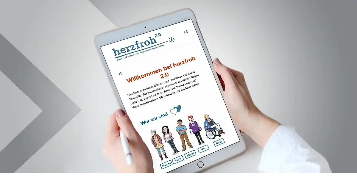 Das Teaserbild zeigt die Webseite herzfroh 2.0 in einem Tablet, das von zwei Händen gehalten wird. 